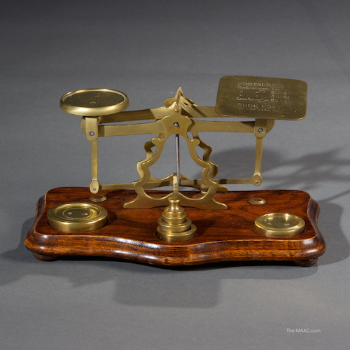 Mahogany and brass postal scale and weights with letter and book rates for 1915. Brass and mahogany, England, 1915. L: 10″ D: 6″ H: 5″