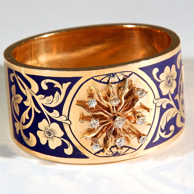 Wide gold bangle with blue floral enamel design and diamonds accenting a sculpted gold flower. USA or England, circa 1900. W: 1-1/2″