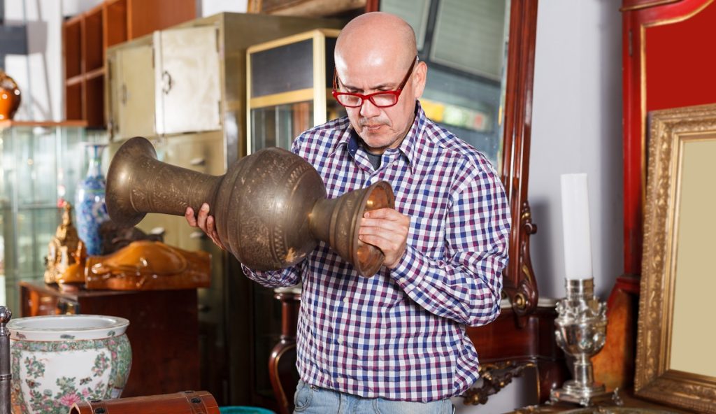 Middle-aged man examines antique vase at antique gallery